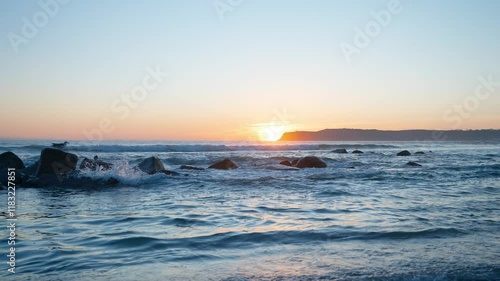 A beautiful sunset on the coast of California with a seagull perched on the rocks as the waves come crashing in. photo