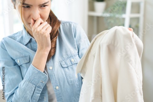 Asian young housewife woman having bad smelling clothes hand holding breath nose with finger, sniff smelly dirty stinky musty, look disgusting from clothes after washed, laundry out of machine at home