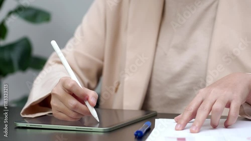 Woman typing work on laptop and checking work on paper as well