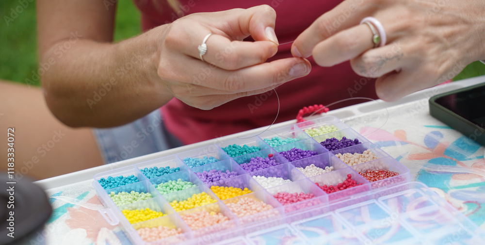 Fototapeta premium Young woman beading colorful bracelets outdoors in a park