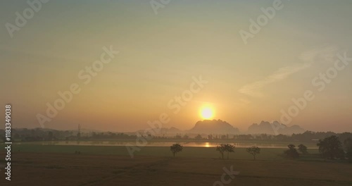 High angle shot of golden sunlight shining through vast rice fields and tall mountains behind. Reflection on golden rice fields. Sunlight shining through rice fields. Beautiful scenery.