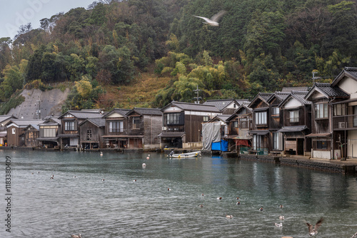 A tranquil autumn scene of the fishing village of Ine in Kyoto, captured during a light rain shower that gently falls over the serene landscape. The traditional 