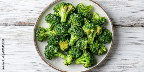 Obraz na płótnie Delicious homemade roasted broccoli seasoned with salt and pepper arranged on a plate atop a white wooden surface. Enjoy this flavorful homemade roasted broccoli from a top view perspective. w salonie