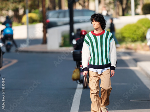 Portrait of a handsome Chinese young man with black and blue striped sweater walking in the street,  young guy with black curly hair in urban background. male fashion, cool Asian young man lifestyle. photo