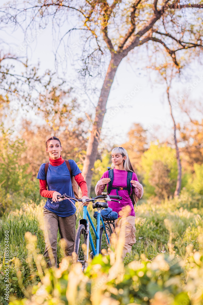 Two young women walking with bicycle in nature enjoying sustainable lifestyle Two young women walking with bicycle in nature enjoying sustainable lifestyle