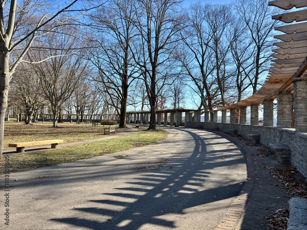 Curved pathway with benches and a stone pergola in a tree-lined park Curved pathway with benches and a stone pergola in a tree-lined park