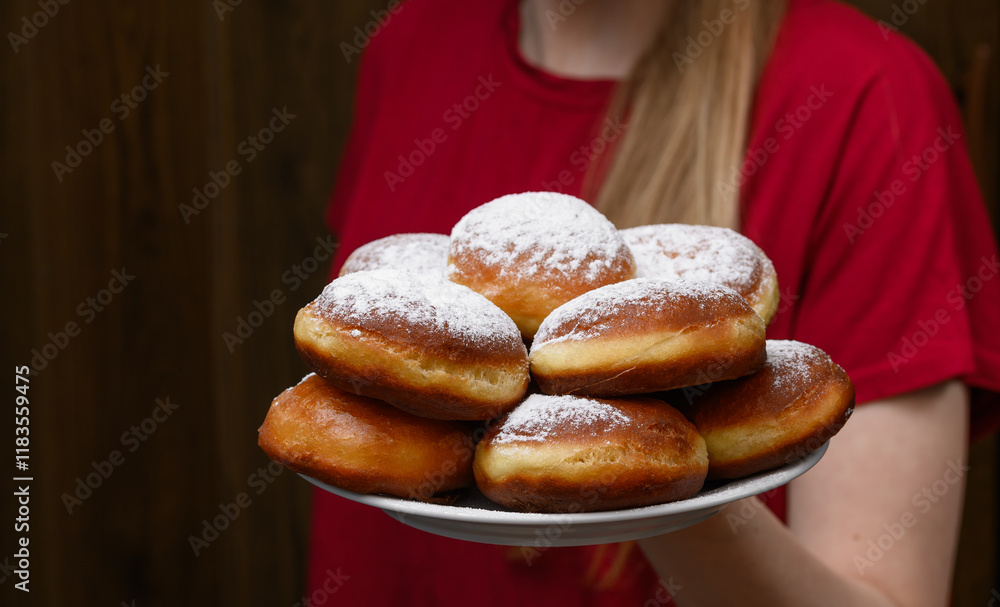 Obraz premium Kobieta trzymająca pączki na talerzu tradycyjnie z cukrem pudrem, prawdziwe domowe pączki drożdżowe 
