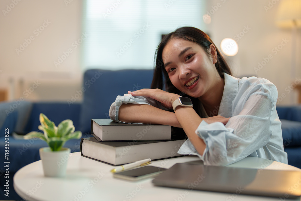 Happy student smiling while leaning on a stack of books, with a laptop and smartphone on the table, celebrating success in online learning from the comfort of home Happy student smiling while leaning on a stack of books, with a laptop and smartphone on the table, celebrating success in online learning from the comfort of home