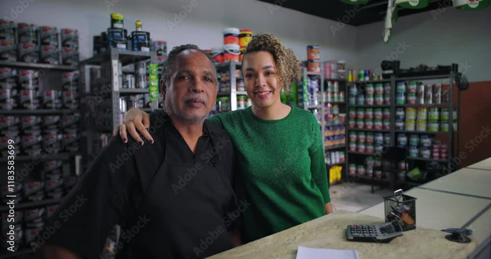 Father and daughter standing together at the counter in their family owned hardware store, shelves of paint cans and supplies in the background, showing unity and pride