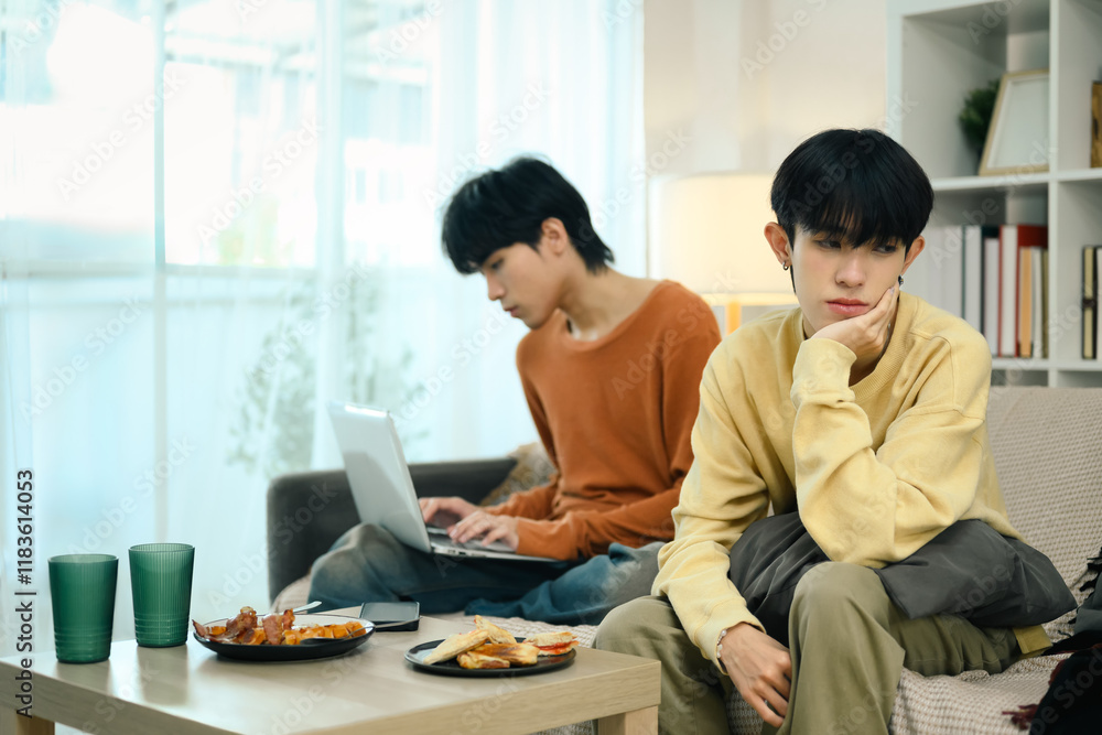 Young gay couple in conflict sitting on couch at home. Disagreement in relationships concept