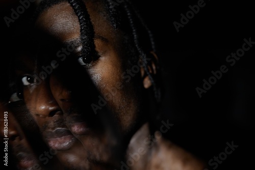 Portrait of African American man looking with piercing stare at camera hiding face in deep dark shadow covering half his face posing in dark studio, double exposure effect, copy space photo