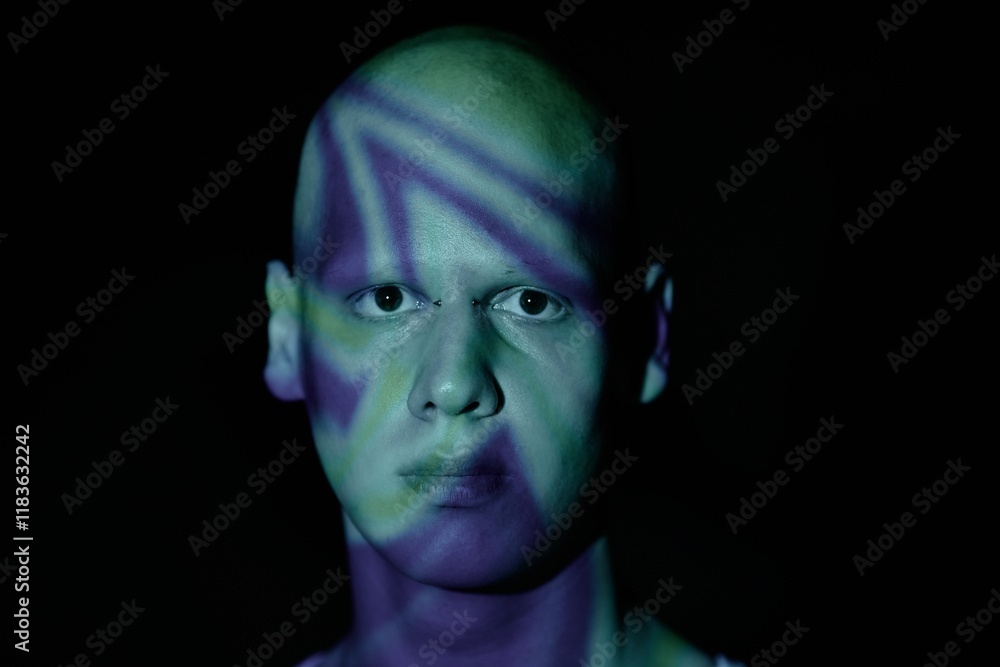 Portrait of emotionless black eyed man with bald head looking at camera with piercing stare while standing in blue light of projector in darkness, copy space Portrait of emotionless black eyed man with bald head looking at camera with piercing stare while standing in blue light of projector in darkness, copy space