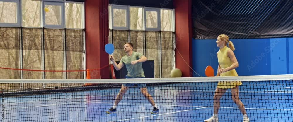 A man and a woman playing pickleball on a blue, inside court
