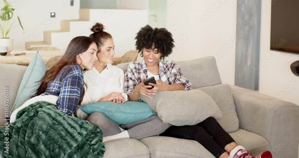 Women friends laughing together on sofa, sharing moments on smartphone at home