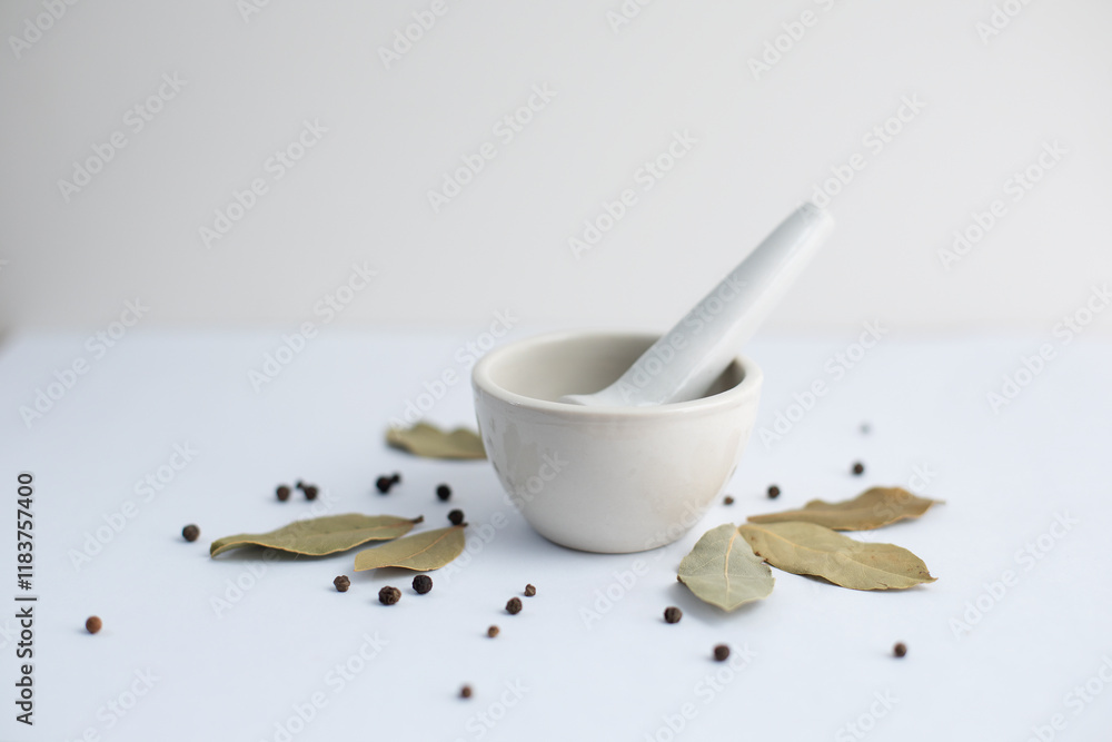 White mortar with black pepper and bay leaves on a white background. White mortar with black pepper and bay leaves on a white background.