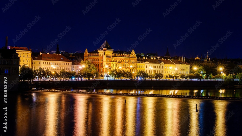 Naklejka premium A breathtaking long exposure photo of Prague, Czech Republic at night, showcasing the Vltava River, Prague Castle, and National Theatre, all under a clear, starry sky.