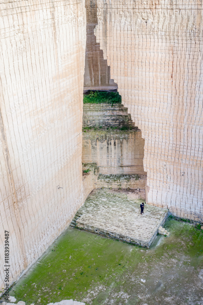 An impressive view of the intricate carvings and stone with a person in the background that serves as a comparison with the grandeur of Lithica Sandstone Quarries, near of Ciutadella, Minorca, Spain.