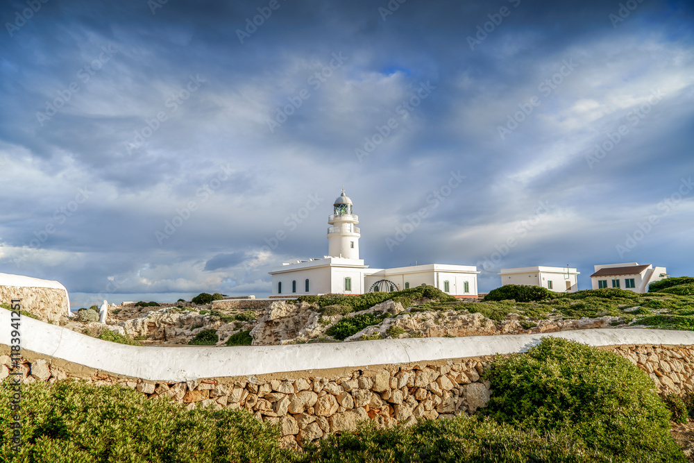 View of the lighthouse of Cap de Cavalleria on the north coast of Menorca (Balearic Islands) during a summer day with dramatic cloudy sky, Minorca, Spain