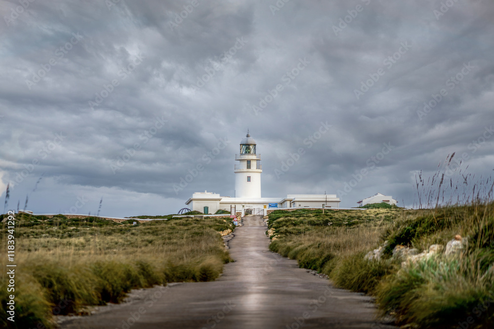 View from the road of the Cap de Cavalleria lighthouse on the north coast of Menorca (Balearic Islands) during a summer day with dramatic cloudy sky, Minorca, Spain