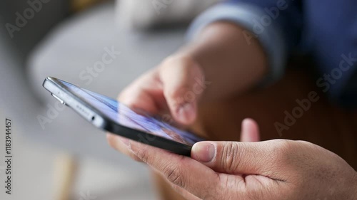 Close up of male hands holding mobile phone sitting on sofa at home. Man uses smartphone, browses social media, scrolls searches for information on the internet, online web user of technology
