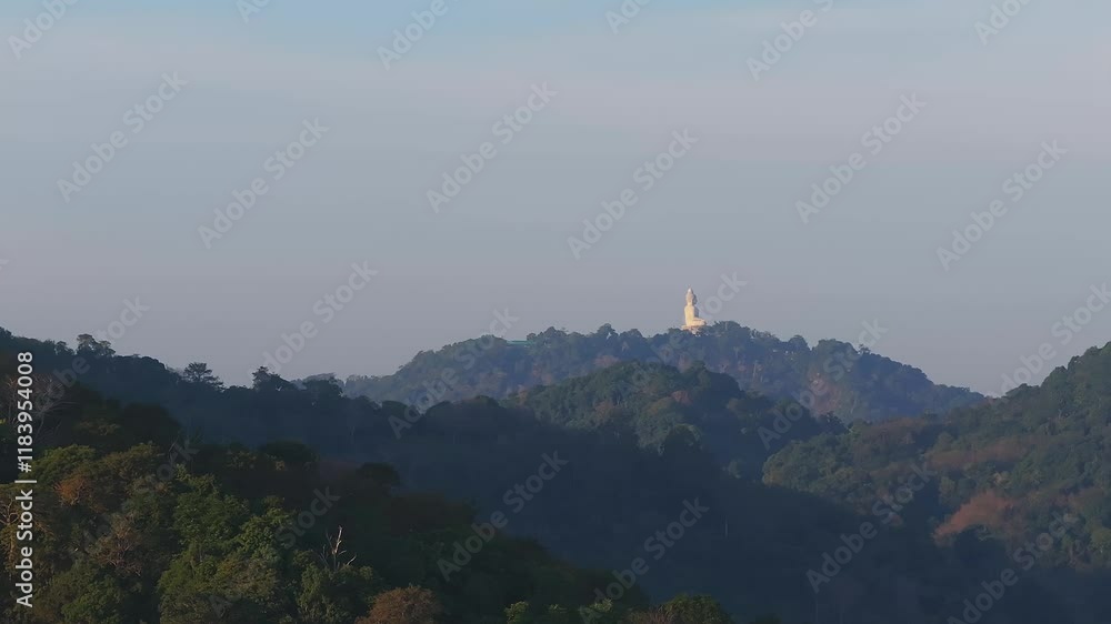 Serene aerial view of the Big Buddha statue on Nakkerd Hill, surrounded by lush forests, rolling hills, and a clear sky in Phuket, Thailand.