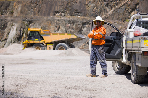 Man in high visibility clothes standing with arms crossed beside ute on mine site photo