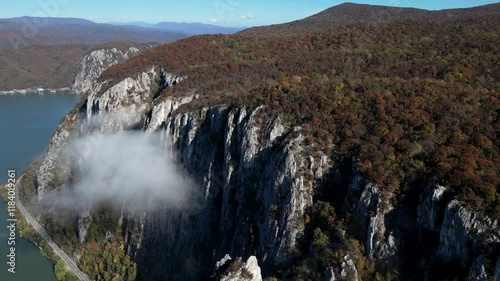 Scenic mountain cliffs with autumn foliage and misty clouds overlooking a serene river in a peaceful natural setting