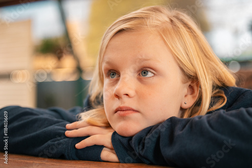 Close up portrait of pre-teen boy with long blond hair and blue eyes resting chin on hands looking photo