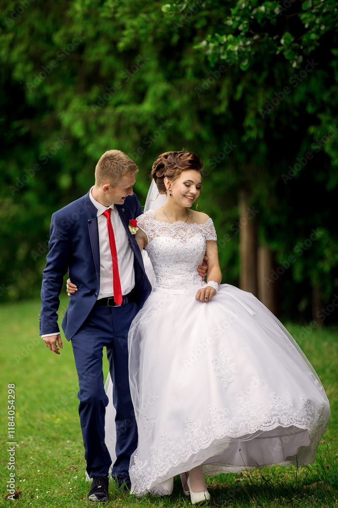 A bride and groom are walking together in a park. The bride is wearing a white dress and the groom is wearing a blue suit A bride and groom are walking together in a park. The bride is wearing a white dress and the groom is wearing a blue suit
