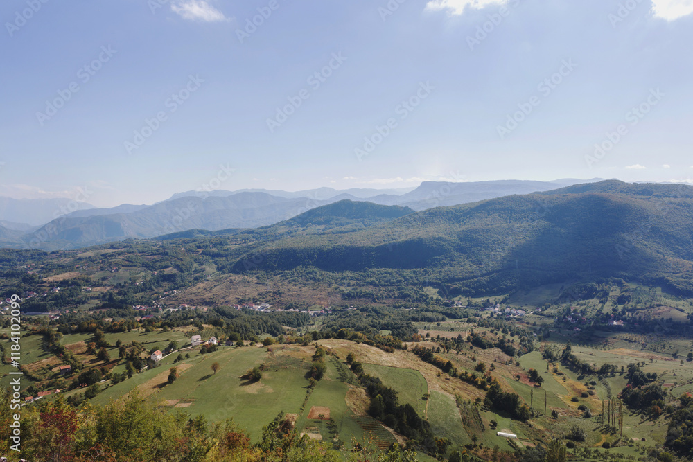 Panoramic view of a mountainous village nestled in a green valley with a blue sky overhead Panoramic view of a mountainous village nestled in a green valley with a blue sky overhead