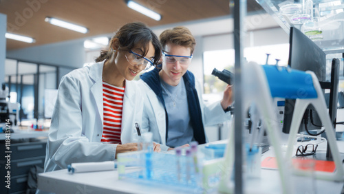 Fotografía Molecular Biology Students Conducting Research in a Lab, Looking at DNA Sample Under a Microscope in an Applied Science Course in College
