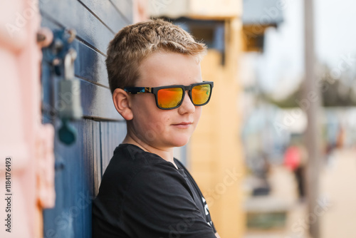 Boy in sunglasses leans on colourful beach wall, exuding a carefree, relaxed vibe photo