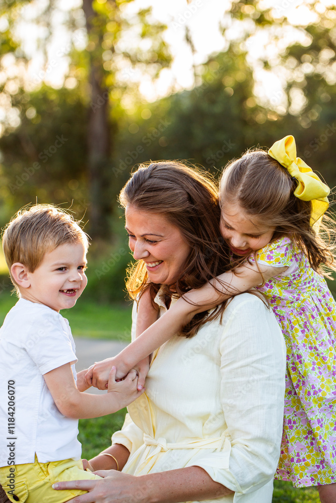 Happy mum with her two children daughter hugging her in golden evening light outdoors Happy mum with her two children daughter hugging her in golden evening light outdoors