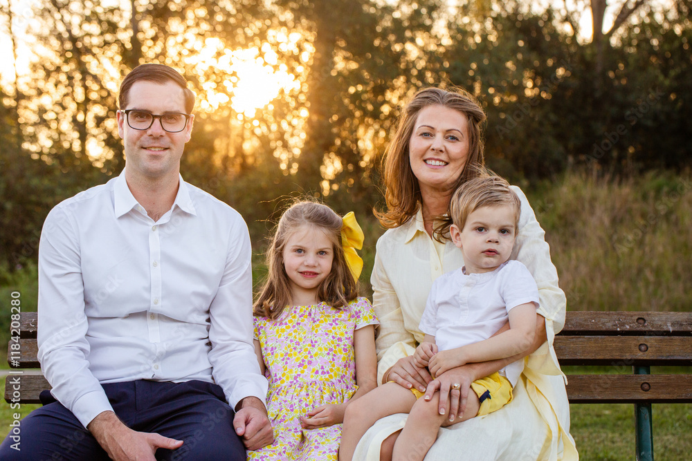 Portrait of family of four with young kids sitting together on park bench at sunset Portrait of family of four with young kids sitting together on park bench at sunset