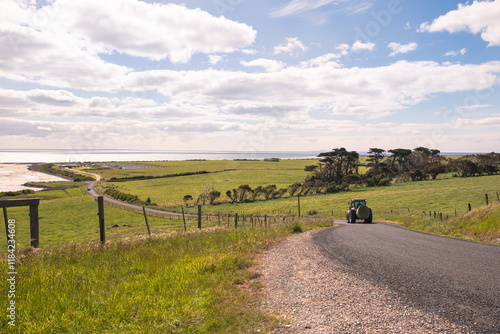 Farm tractor with hay bale driving on the coastal country road. photo