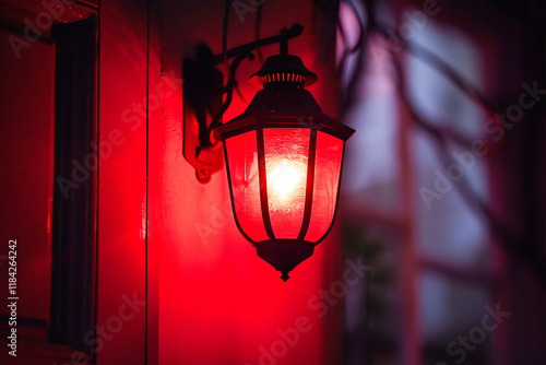 A red outdoor lantern glows brightly at night, casting a warm light on the surrounding wall.