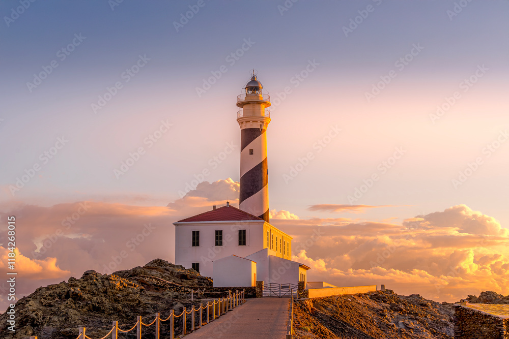 The iconic Favaritx Lighthouse at sunrise, set on the northeastern coast of Menorca near Mahon, Balearic Islands, Spain, against a backdrop of serene Mediterranean waters