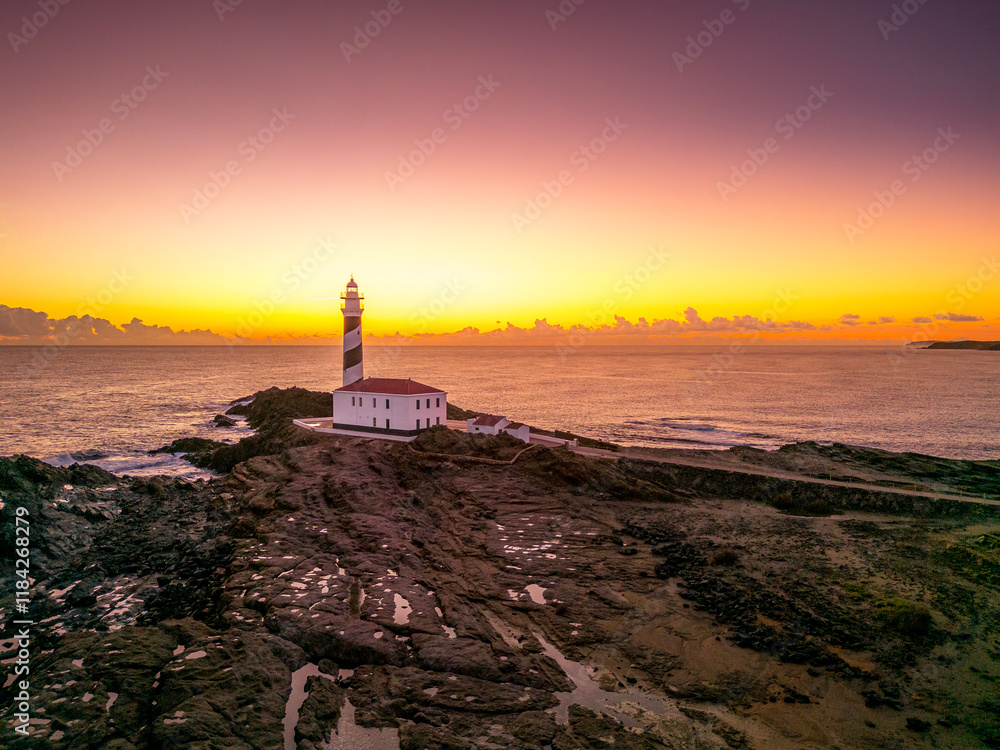 Scenic view of Favaritx Lighthouse at sunrise, located near Mahon in Menorca, Balearic Islands, Spain, with the golden light reflecting on the Mediterranean waters
