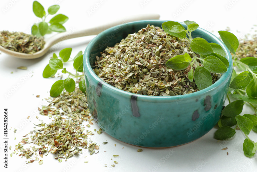 Dried oregano in bowl, spoon and green leaves on white table, closeup Dried oregano in bowl, spoon and green leaves on white table, closeup