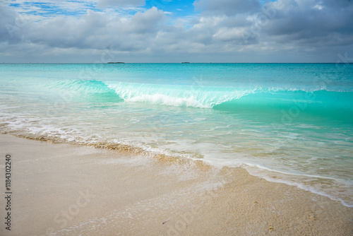 Fototapeta Naklejka Na Ścianę i Meble -  Gentle Wave Crashing on a Pristine Sandy Shore with Turquoise Waters and a Cloudy Sky