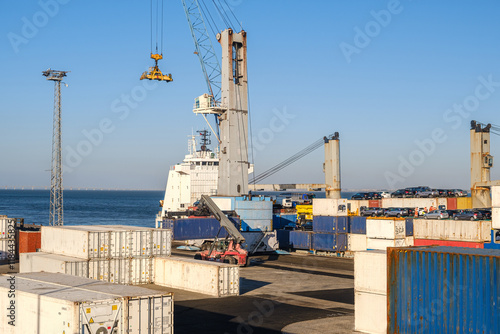 Obraz na płótnie Cargo port busy with loading a bulk carrier, crane and reach stacker w salonie