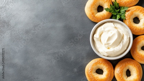 Six bagels arrayed around bowl of cream cheese on grey surface with sprig parsley photo