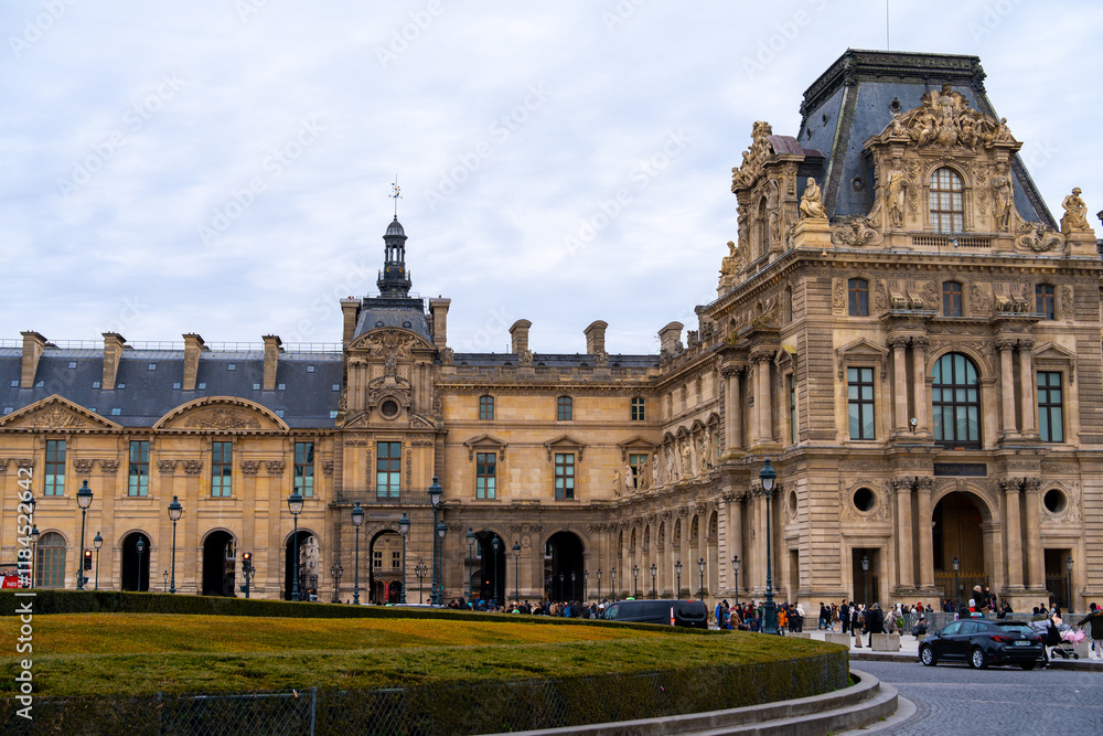 Visitors explore the historic architecture and courtyard of the Louvre Museum in Paris during a cloudy afternoon Visitors explore the historic architecture and courtyard of the Louvre Museum in Paris during a cloudy afternoon