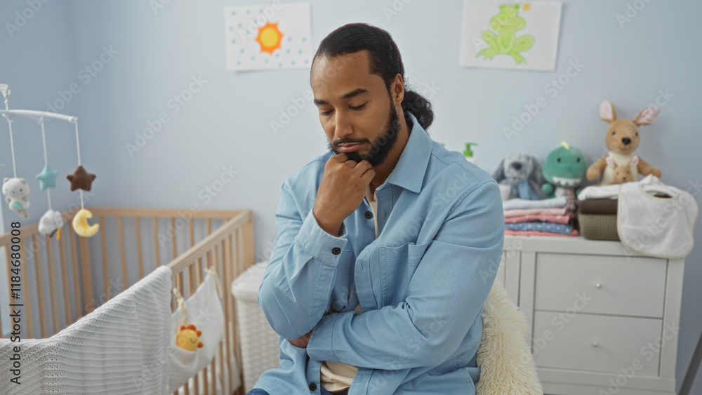 Fototapeta premium Young man with beard seated in a bedroom beside a cradle, appearing thoughtful in the serene, softly lit interior space.