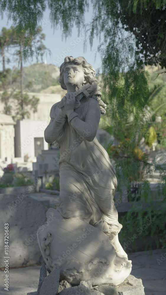 Angelic statue praying in a cemetery garden with tombstones in the background Angelic statue praying in a cemetery garden with tombstones in the background