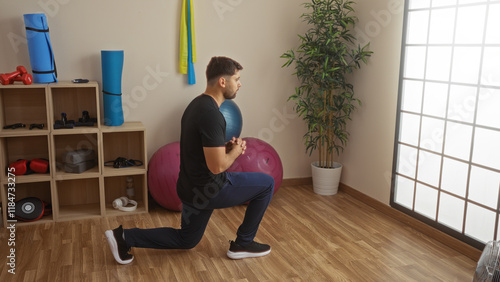 Young man performing lunge exercise in gym surrounded by fitness equipment, showcasing dedication to a healthy lifestyle in a well-lit indoor space. photo