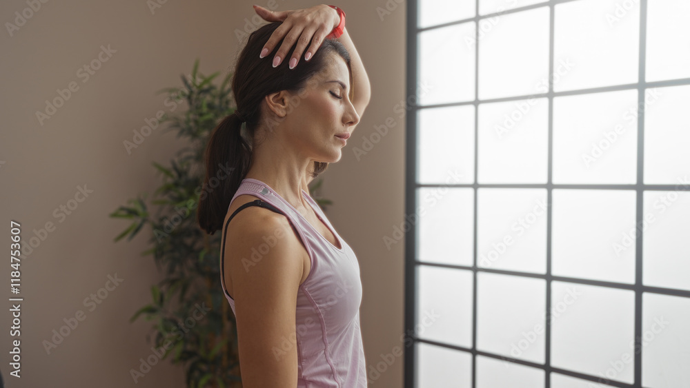 Woman stretching indoors at a gym with soft lighting and serene expression, capturing calmness and focus in a modern sports center setting. Woman stretching indoors at a gym with soft lighting and serene expression, capturing calmness and focus in a modern sports center setting.