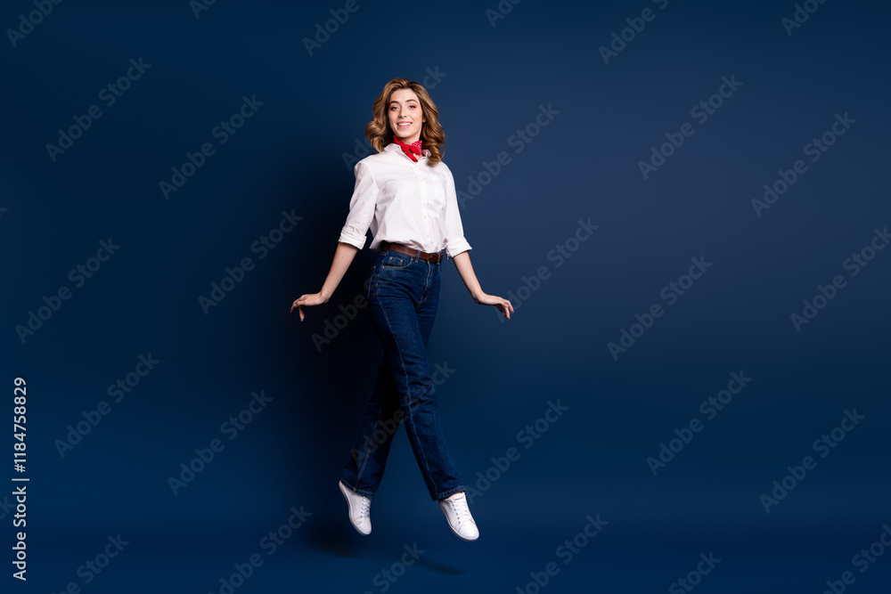 Joyful young woman jumping in stylish ensemble with dark blue background, exuding elegance and charm Joyful young woman jumping in stylish ensemble with dark blue background, exuding elegance and charm