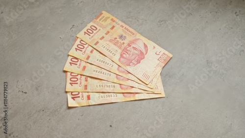Mexican banknotes worth 100 pesos each are fanned out on a concrete surface, showcasing the detailed design of mexican currency.