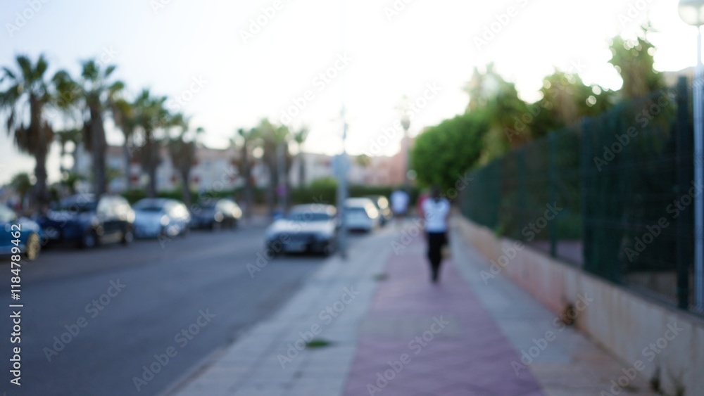 Blurred outdoor street scene with defocused cars, palm trees, and a woman walking on a sidewalk in the background